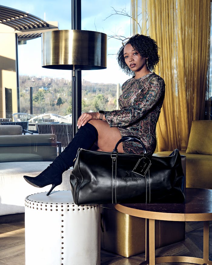 Fashion-forward woman sitting in a chic room with a stylish leather bag, embodying modern elegance.