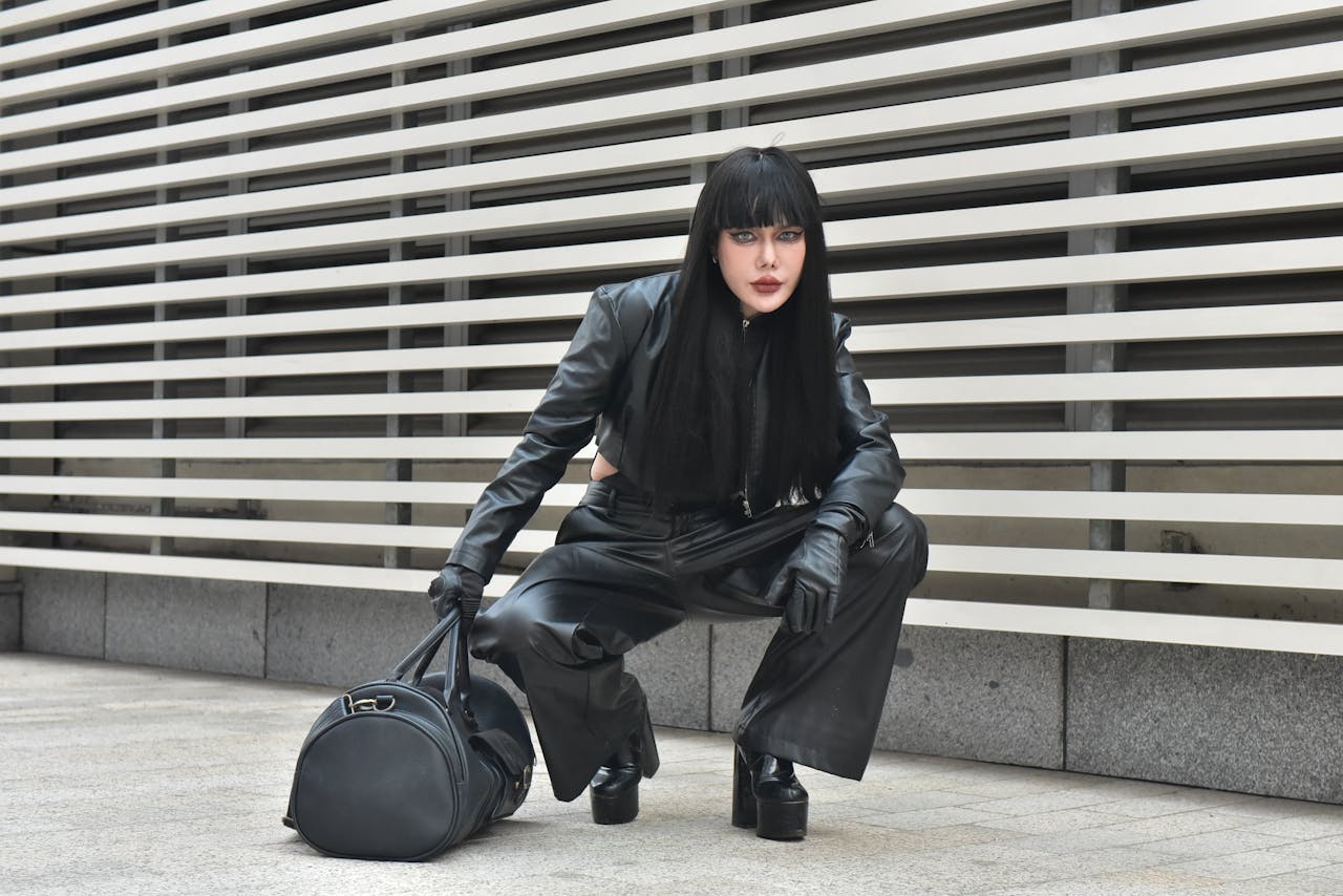 Striking pose of a model in black leather outfit outdoors, showcasing urban fashion.